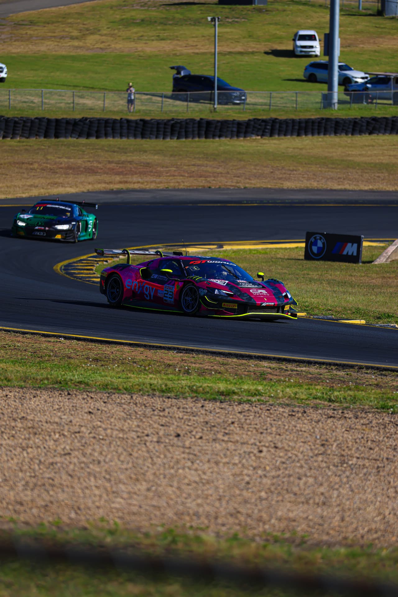 Pink Ferrari GT car leading a green Audi through a corner