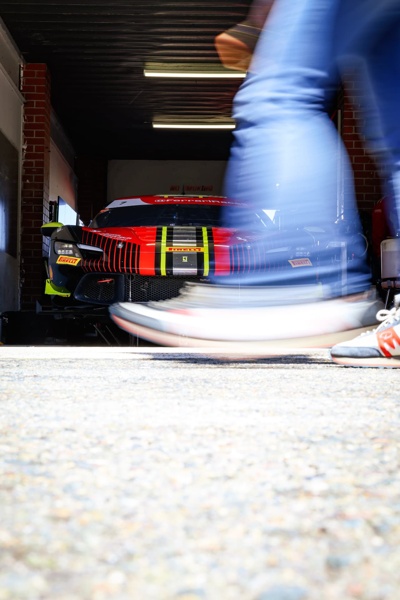 Ferrari in a pit garage framed by a person walking past