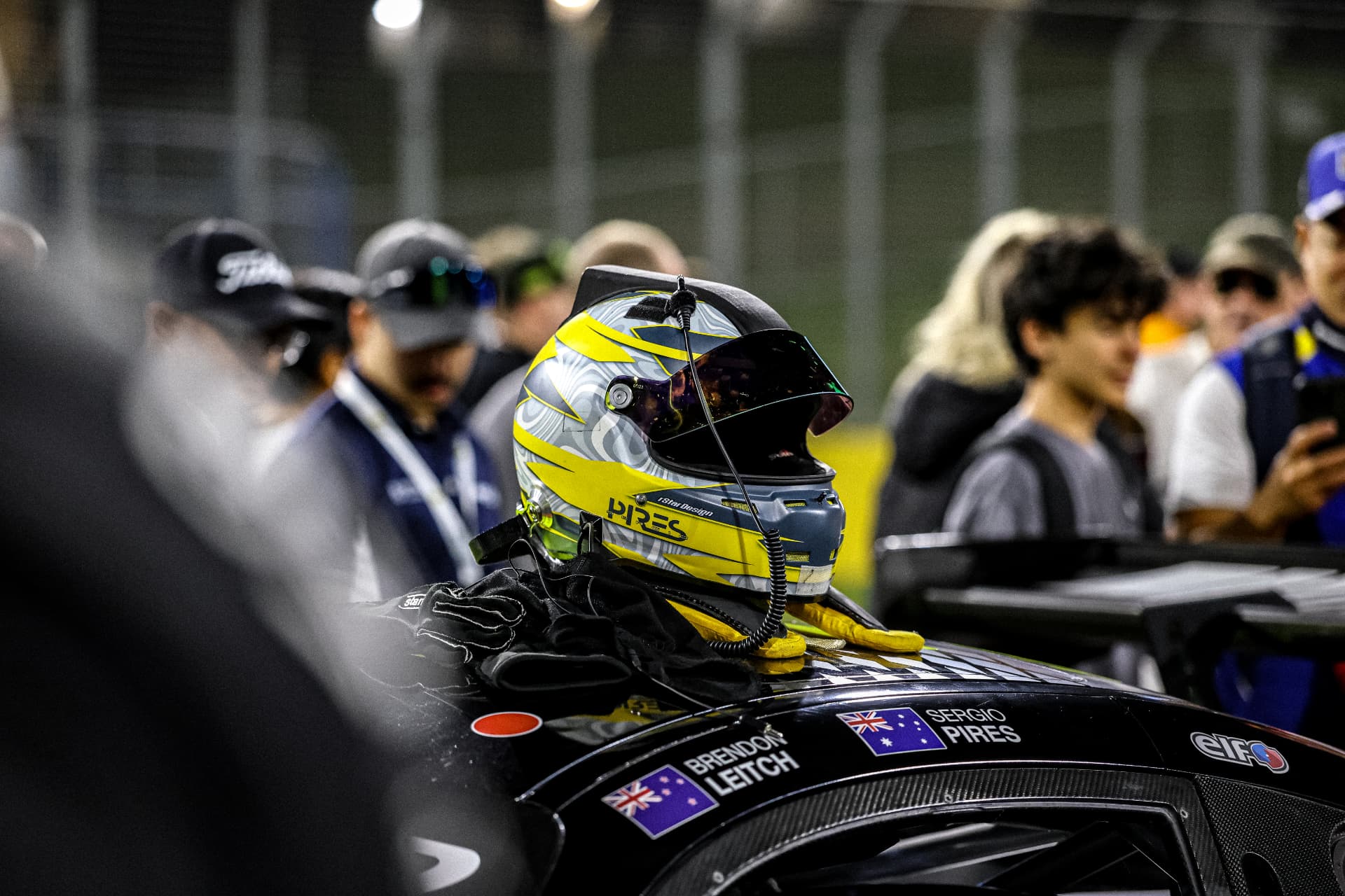 Yellow driver helmet and gloves resting on a black GT car on the grid