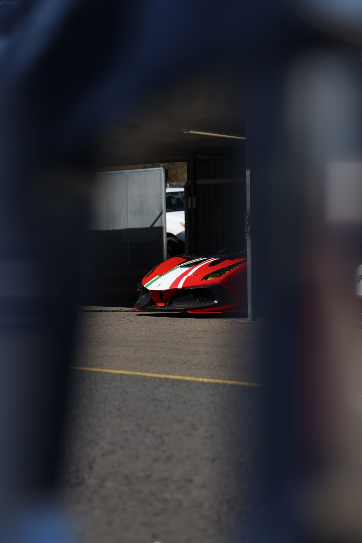 Red Ferrari glimpsed through a blurred foreground at the circuit