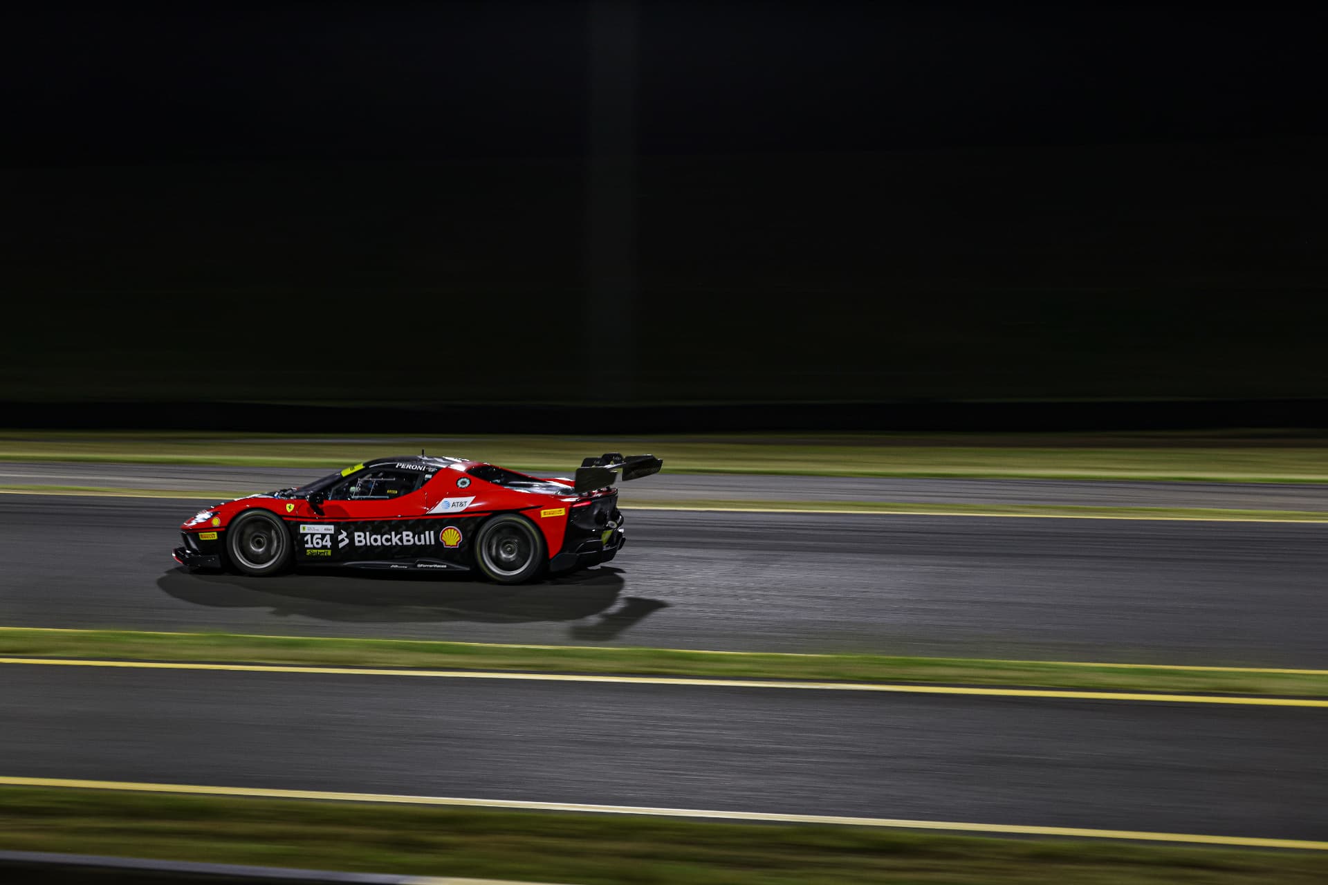 Red BlackBull Ferrari #164 streaking down the straight at night