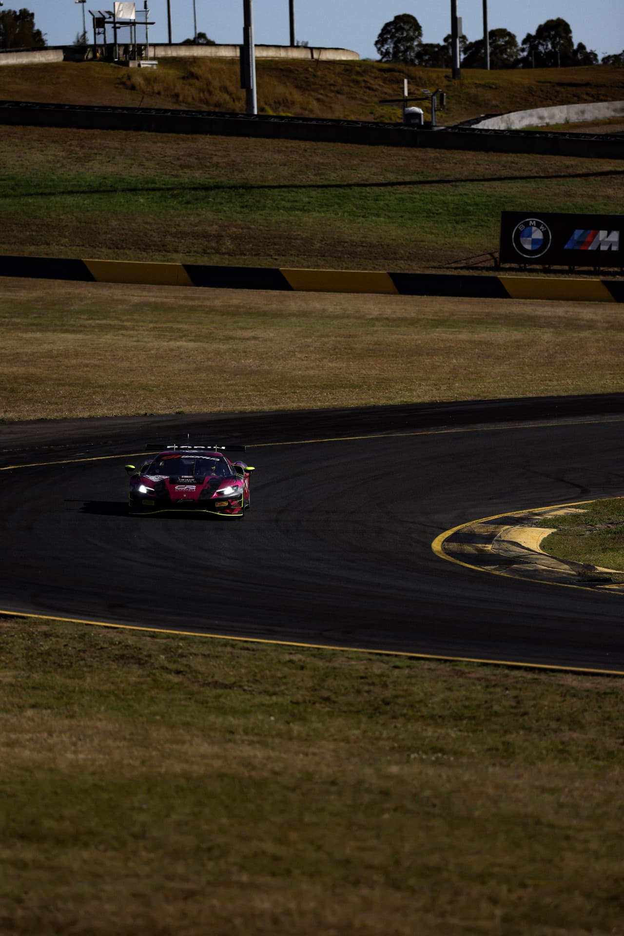 Pink and black Ferrari approaching a shaded circuit corner