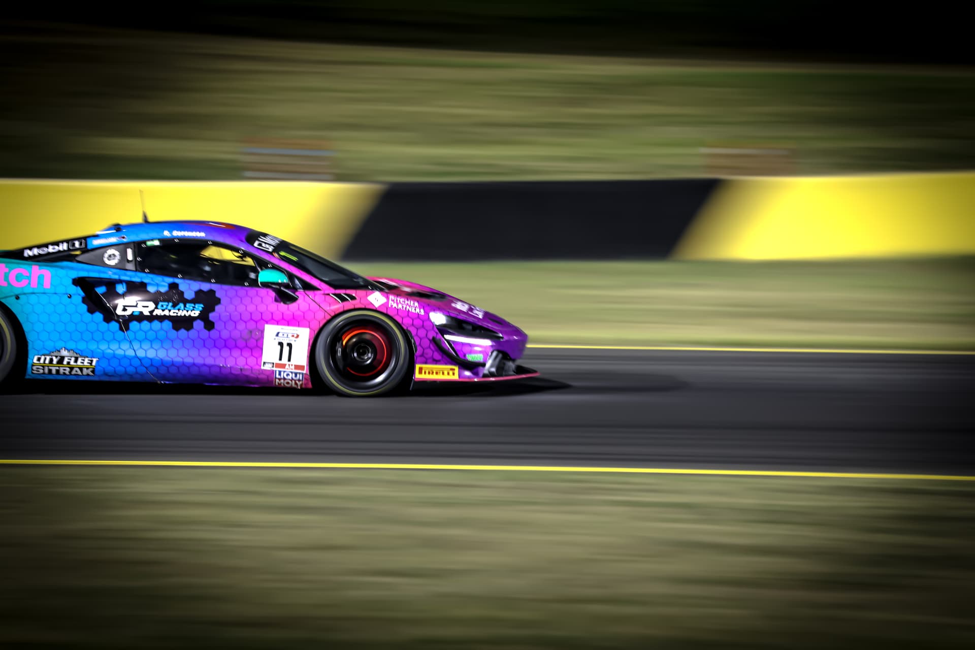 Purple and blue McLaren GT4 #11 panned past yellow barriers