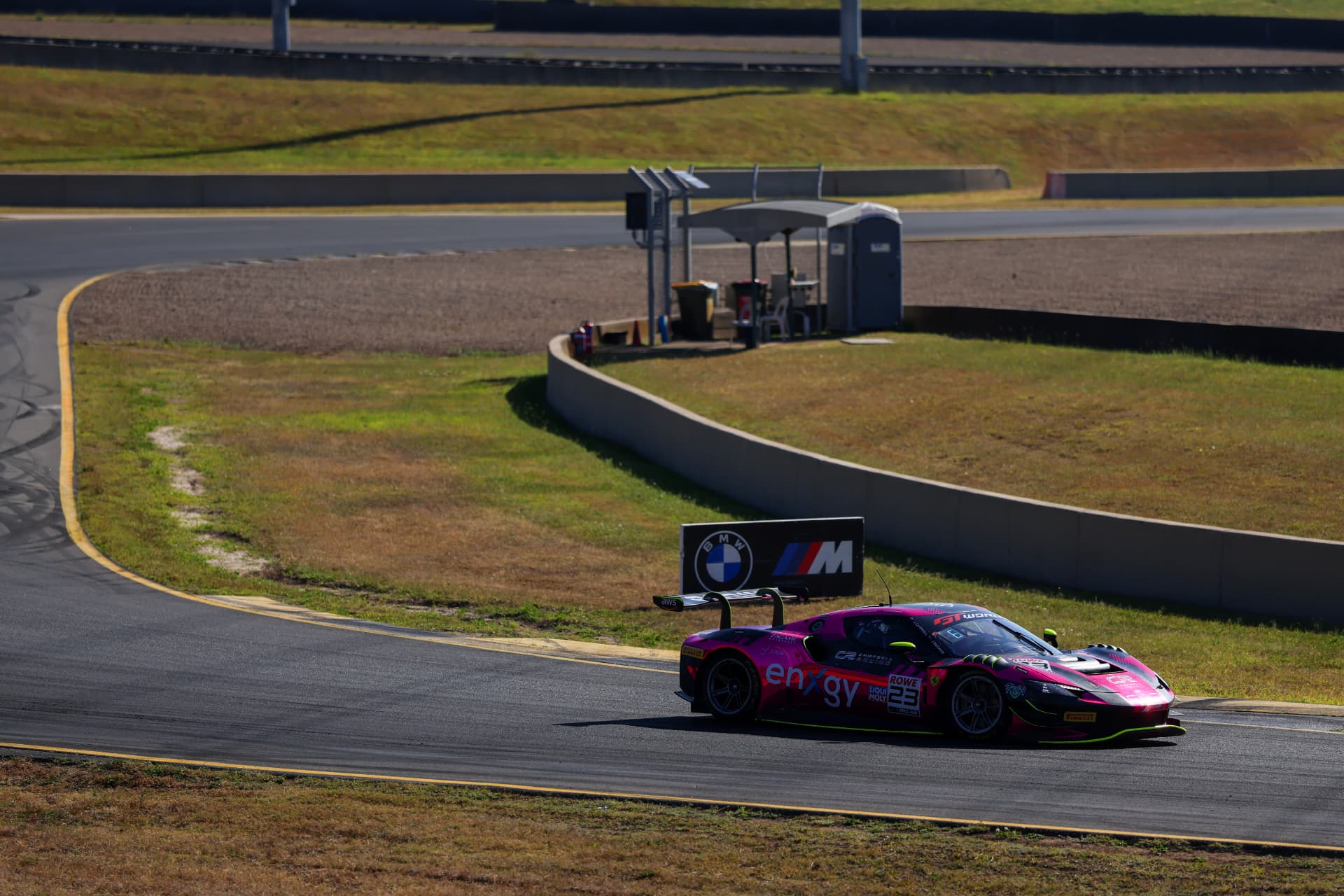 Pink Ferrari GT car crossing a sunlit circuit bend