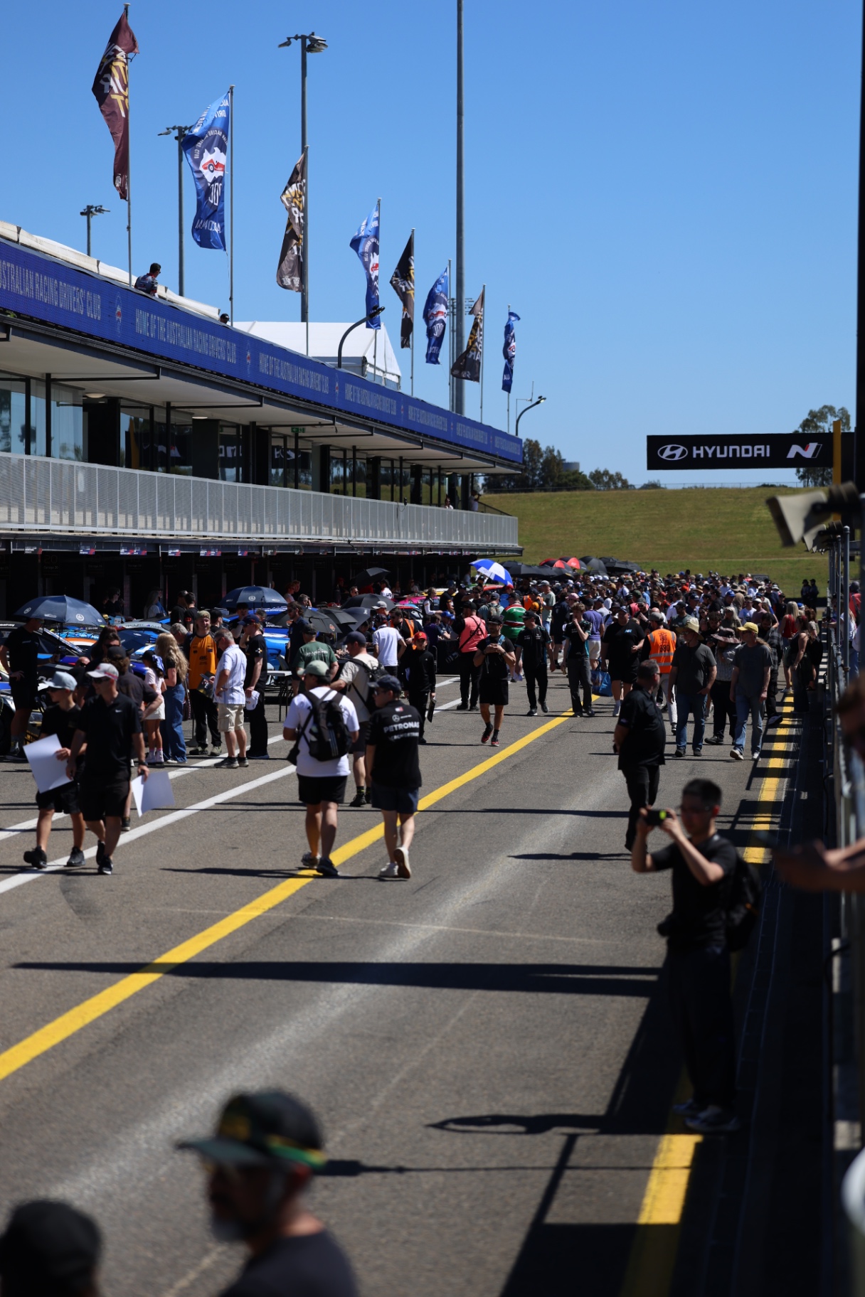 Spectators walking along the pit straight beneath club flags